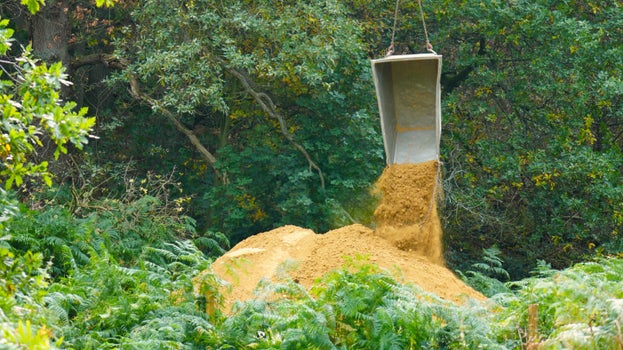 Tonnes of yellow stone are dropped from a small skip connected to the bottom of a helicopter